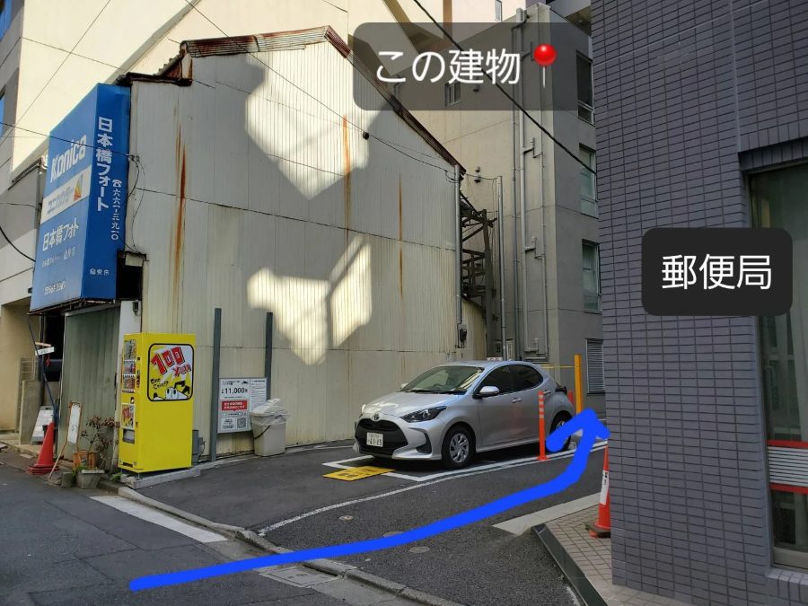郵便局の裏のタイムズカーシェアの駐車場と、その奥に見える建物